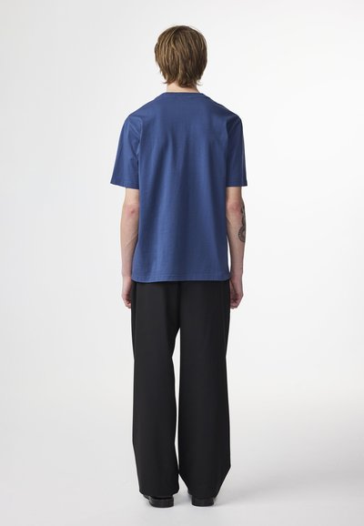 Blå bomulls t-shirt med korta ärmar och avslappnad passform, i kombination med vida svarta byxor. Enkelt utformad, utan synliga mönster eller detaljer.