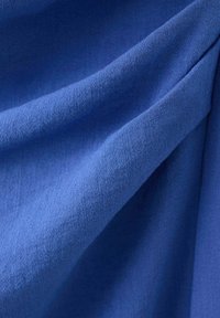Blauwe stof met zichtbare weefstructuur, met zachte plooien en schaduwen die het gladde, licht gestructureerde oppervlak benadrukken.