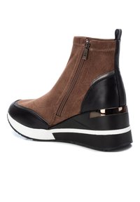 Botín de ante marrón con detalles en cuero negro, cremallera lateral, suela de cuña blanca y negra, y un detalle metálico en el tacón.