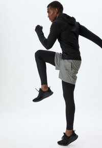 Sportstøj bestående af en sort langærmet hættetrøje, grå shorts og sorte leggings. Sorte sneakers med strukturerede såler fuldender looket.