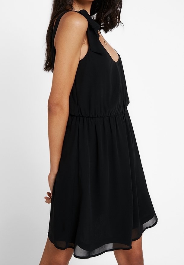 Robe noire sans manches avec un décolleté arrondi, un détail en nœud à l'épaule, une taille élastique, et une silhouette évasée fluide avec un ourlet transparent.
