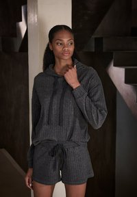 Grauer Ripp-Hoodie mit Kordelzügen, kombiniert mit passenden Shorts. Weicher Stoff, lockere Passform und elastischer Bund. Einfaches Design.