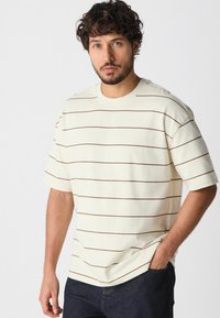 Crème T-shirt met korte mouwen en bruine horizontale strepen, gemaakt van zachte stof. Heeft een ronde hals en een relaxte pasvorm.