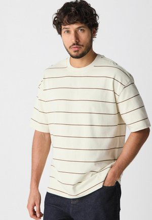 T-shirt crème à manches courtes avec des rayures horizontales marron, fabriqué en tissu doux. Doté d'un col rond et d'une coupe décontractée.