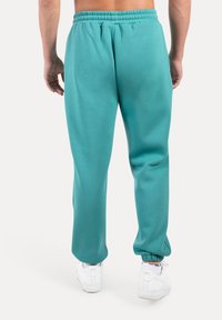 Turkosa mjukisbyxor med resår i midjan och vid anklarna, tillverkade av ett mjukt tyg. Bärs med vita sneakers.