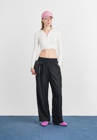 Λευκό κοντό πουλόβερ, μαύρο χαλαρό παντελόνι, ροζ καπέλο και ροζ παπούτσια, με μία μικρή μαύρη τσάντα. Λείες υφές και χαλαρός σχεδιασμός.