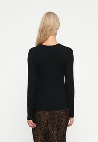 Sort langærmet top med et tætsiddende design, ribbet tekstur og rund halsudskæring, parret med en leopardmønstret nederdel.