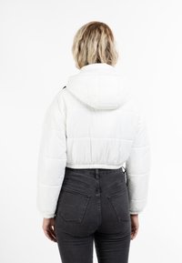 Kappad vit puffjacka med huva, ribbad midjeresår och elastiska ärmslut; slät textur och kviltade designdetaljer.