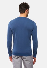 Blå långärmad tröja med en strukturerad stickad mönster, rundad halsringning och åtsittande mudd är kombinerad med ljusgrå byxor.