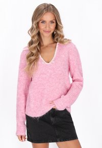 Rosa Strickpullover mit V-Ausschnitt, weißen Akzenten und Perlenverzierungen. Verfügt über ein strukturiertes Muster und lange Ärmel, kombiniert mit einem schwarzen Denim-Rock.