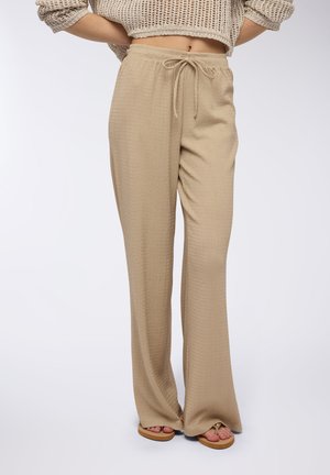 Pantaloni beige, a gamba ampia e texture, con vita elastica e cordoncino. Il tessuto presenta un motivo discreto e arriva sopra la caviglia.