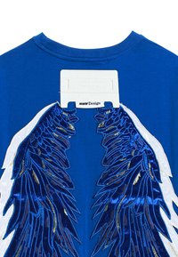 Camiseta de algodón azul con grandes diseños de alas en relieve azules y blancos, con una etiqueta que dice "MWM Design" en la parte de atrás.