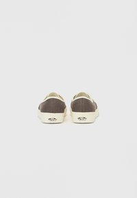 Brune lerret slip-on sko med kremfarget detaljer, med en glatt tekstur og logodetalj på hælen. Sålene er flate og noe hevet.