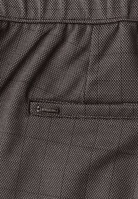 Gros plan d'un pantalon en tissu foncé texturé avec un petit motif à pois blancs et une poche étiquetée "Street One."