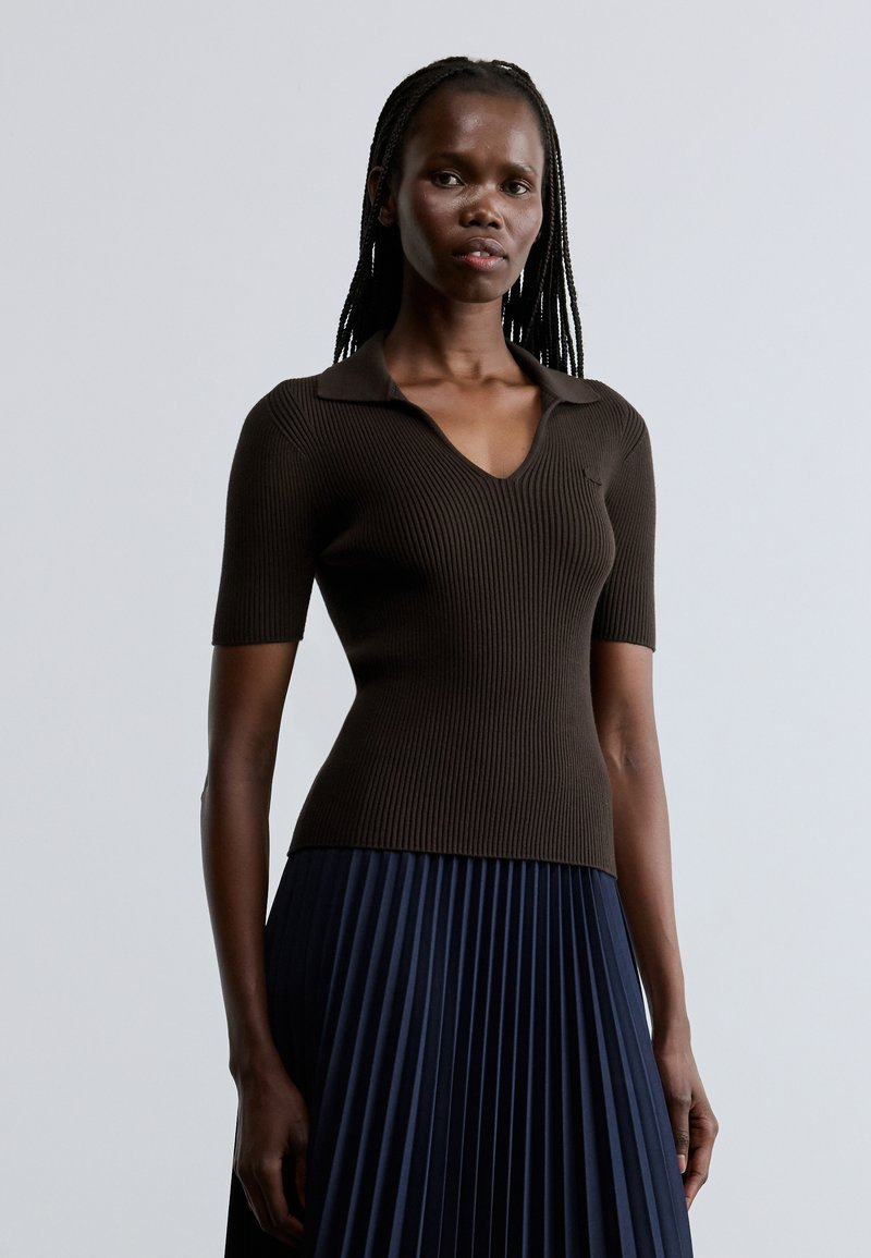 Top marrón de manga corta con textura acanalada y cuello, con diseño de escote en V. Combinado con una falda plisada azul marino para un look en capas.