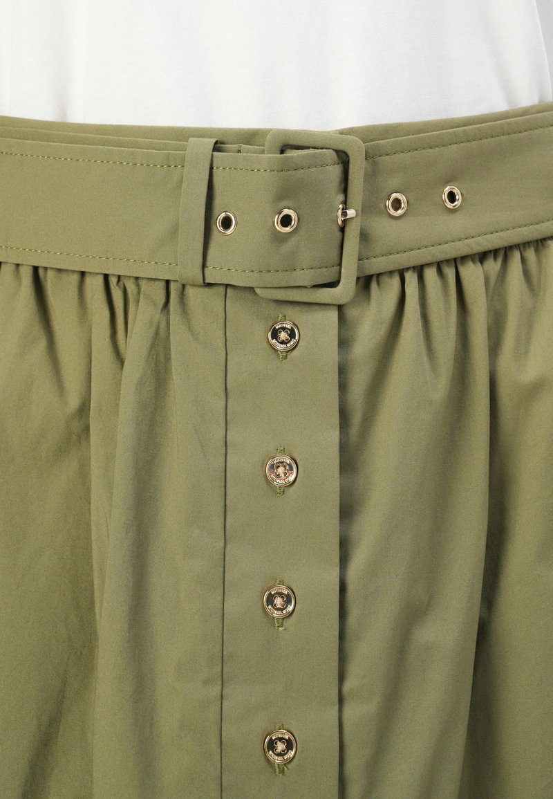 Gonna verde oliva con cintura larga, accessori in oro e bottoni frontali. Presenta una texture arricciata sotto il girovita e una pattina con bottoni funzionale.