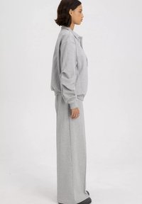 Grijze oversized sweatshirt met een hoge kraag, gecombineerd met bijpassende brede broek. Beide hebben een zachte, gestructureerde stof.