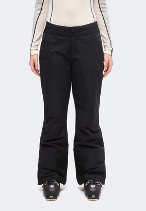 Personne portant un pantalon de ski noir, un haut crème à manches longues avec des manches à motifs et des chaussures de ski noires, debout face à l’avant.