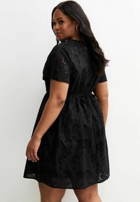 Black dress featuring a textured fabric with floral cutouts, short sleeves, a cinched waist, and a flared A-line skirt.