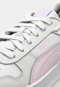 White sneaker with pink accents, made of smooth leather. Features flat laces, stitched detailing, and a pink Puma logo on the side.