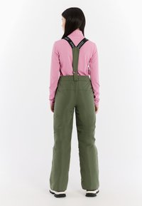 Groene skibroeken met verstelbare zwarte banden, gecombineerd met een lange mouw roze top. Heeft een gladde textuur en een relaxte pasvorm.