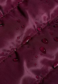 Wodoodporny bordowy materiał z widocznymi kroplami, charakteryzujący się gładką teksturą i lekkim połyskiem, przeszyty łączonymi szwami.