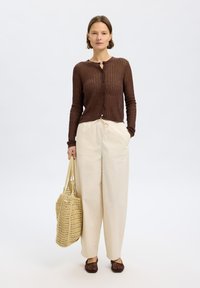 Brun ribbestrikket cardigan med knapper, kremfargede vide bukser, brune vevde slip-on sko og en beige heklet totebag. Enkel, teksturert helhetslook.