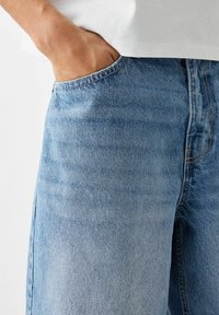 Ljusblå denimjeans med avslappnad passform, synliga sömnadsdetaljer och en sidoficka med en något urblekt textur.