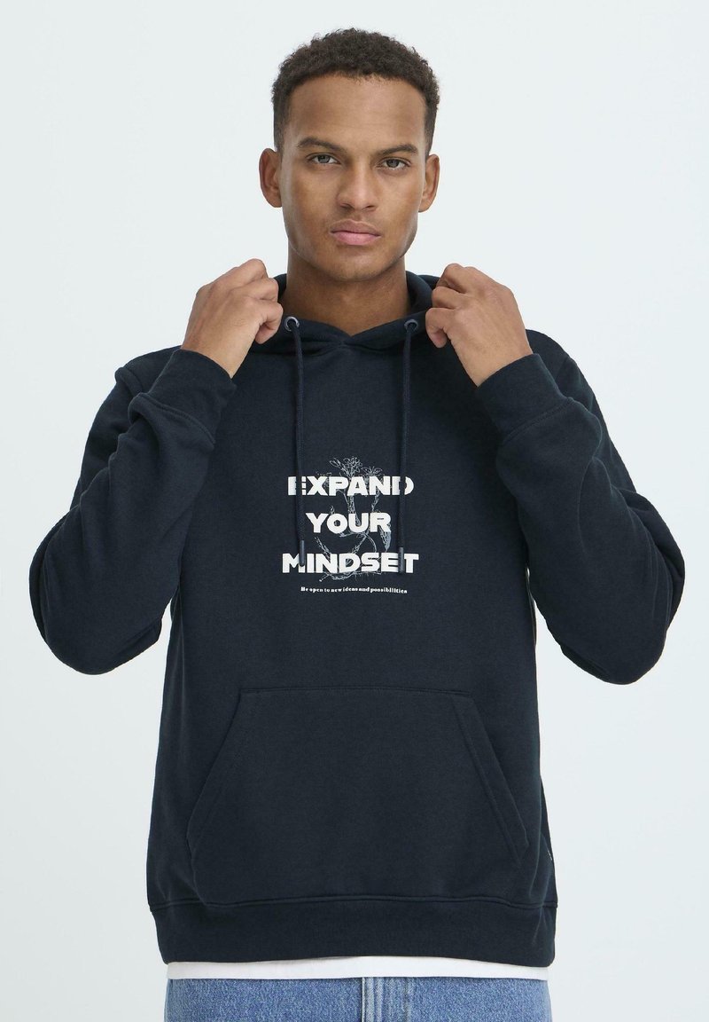 Námornícka mikina s kapucňou vyrobená z mäkkej látky, s predným vreckom a grafickým textovým dizajnom v bielej farbe, ktorý hovorí "ROZŠÍRTE SVOJE MYSLENIE."