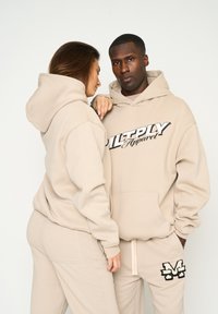 Felpe e pantaloni della tuta beige realizzati in tessuto spesso; le felpe presentano un logo audace; i joggers hanno una tasca e un accento ricamato sulla coscia.