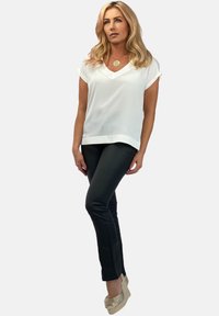 Biała bluzka z krótkim rękawem i dekoltem w kształcie litery V, w połączeniu z dopasowanymi czarnymi spodniami oraz metalicznymi, plecionymi butami na koturnie, tworzy elegancką sylwetkę.