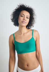Grønn, sømløs bralette med tynne stropper, laget av glatt, elastisk materiale. Tettsittende design, kombinert med hvite truser. Enkel, moderne stil.