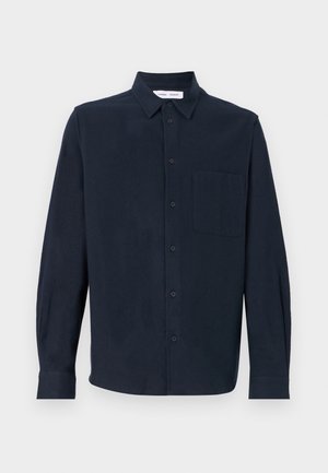 Námořnická modrá dlouhá košile vyrobená z měkké tkaniny, s knoflíkovou přední částí, špičatým límcem a jednou náprsní kapsou.