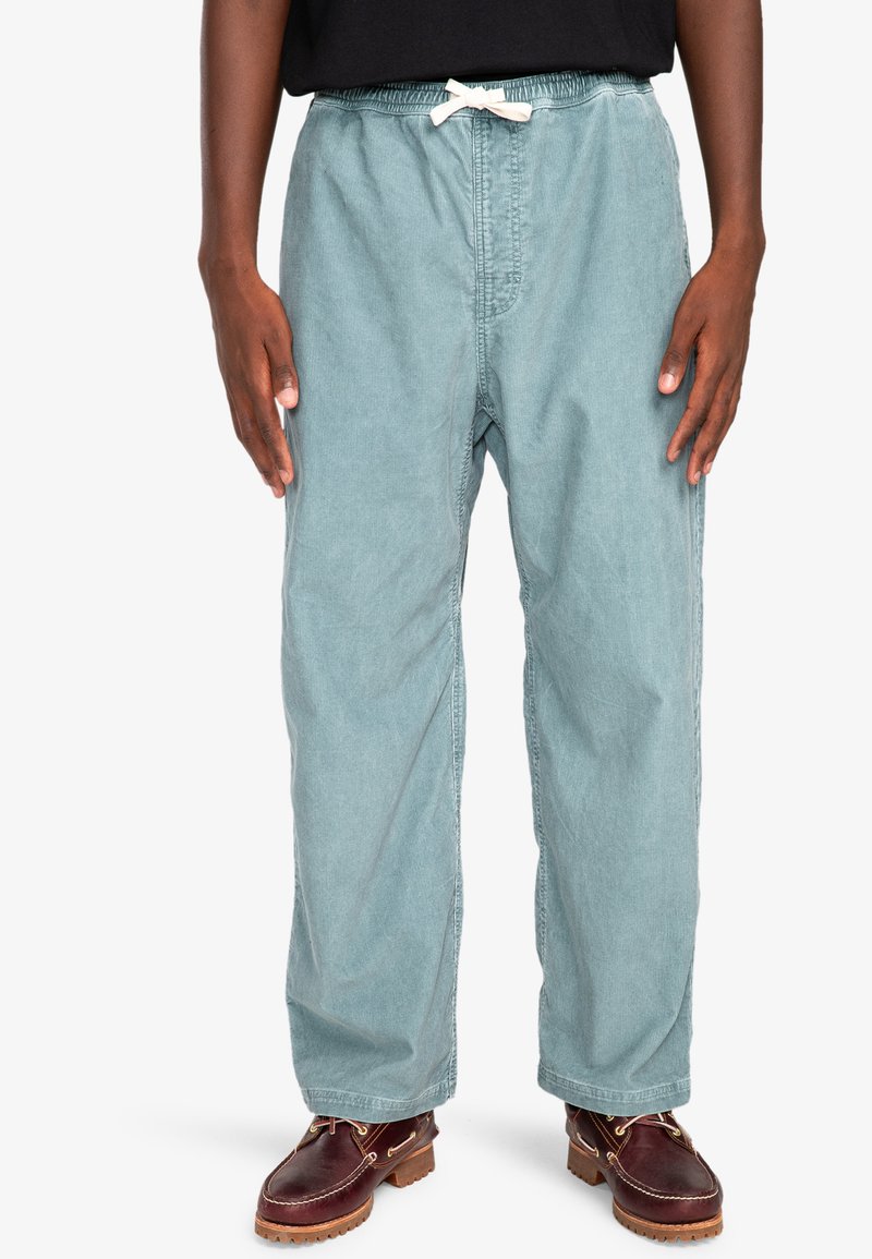 Light teal cotton pants with an elastic waistband and drawstring, featuring a relaxed fit and smooth texture. Worn with brown leather shoes.