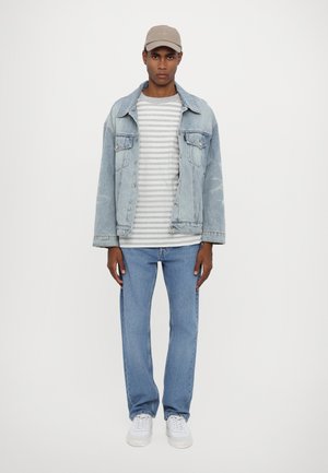 Light blue denim jacket over a gray and white striped t-shirt, paired with light blue jeans and white sneakers. A beige cap completes the outfit.