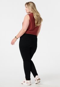 Rode structuurloze mouwloze top gecombineerd met zwarte strakke jeans en witte sneakers. Een dunne gouden armband om de pols; haar gestyled in zachte golven.