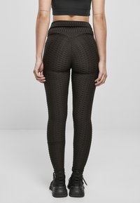 Leggings noirs texturés avec un design ajusté et une taille haute, présentant un motif en grille surélevé et associés à des bottines noires.