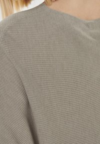 Szary materiał o fakturze z poziomym prążkowaniem, z luźnym dekoltem i miękkim, lekkim wyglądem. Zbliżenie na tkaninę.