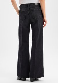 Zwarte wijde broekspijpen jeans met een hoge taille en een gestructureerde denim afwerking. Voorzien van twee achterzakken en een label op de tailleband.