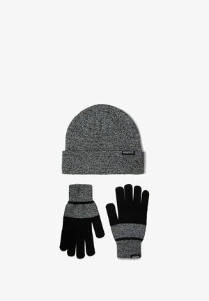 Szürke kötött sapka hajtott széllel és hozzáillő kesztyűkkel. A kesztyű fekete díszítéssel és csíkos mintázattal rendelkezik. Az anyag lágy és texturált.