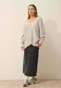 Lichtgrijze oversized trui met een V-hals en ribbeltextuur, gecombineerd met een lange zwarte spijkerrok en meerkleurige sneakers.