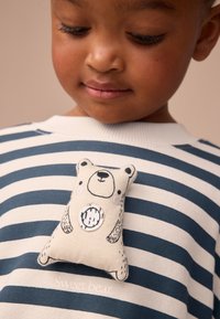 Stribet sweater i marineblå og creme med et patch i form af en bjørn. Patchet har en simpel illustration med sorte detaljer og en rund, syet udsmykning.