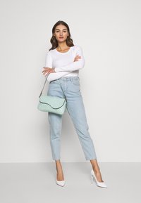 Mintgrüne Handtasche mit einem strukturierten, krokodilgeprägten Design und einem geschwungenen Deckel, kombiniert mit hellblauen, schmal geschnittenen Jeans und einem weißen Langarmoberteil.