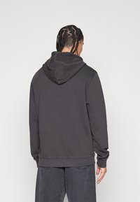 Tummanharmaa huppari, jossa on rento istuvuus, ribatut hihansuut ja helma sekä pehmeä rakenne. Ominaisuuksiin kuuluu suuri takahuppu ja minimaalinen muotoilu.