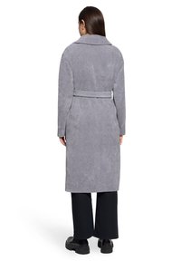 Long manteau gris en tissu texturé, avec un large col et une ceinture assortie nouée à la taille. Fini avec un ourlet droit et des poches latérales.