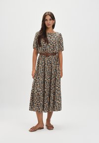 Kwiatowa sukienka midi z ciemnej tkaniny w pomarańczowe i białe wzory, z krótkimi rękawami, z zaakcentowaną talią przy pomocy brązowego paska, zestawiona z beżowymi sandałami.