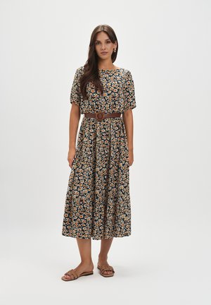 Kwiatowa sukienka midi z ciemnej tkaniny w pomarańczowe i białe wzory, z krótkimi rękawami, z zaakcentowaną talią przy pomocy brązowego paska, zestawiona z beżowymi sandałami.