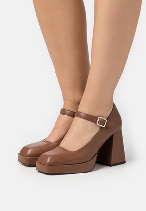Escarpins Mary Jane en cuir marron avec un bout carré, un talon épais et une bride au niveau de la cheville avec une boucle en argent. Texture lisse.