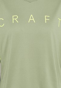 Ljusgrön atletisk tröja med v-ringning och texturerad tyg. "CRAFT" tryckt i klar gul färg över framsidan.