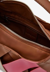 Brown leather bag interior with a zip closure, featuring a smooth texture and a logo tag. Accent colors include pink.